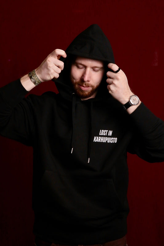 Karhupuisto Film Festival black unisex hoodie with Lost in Karhupuisto print worn by a man against a dark red background