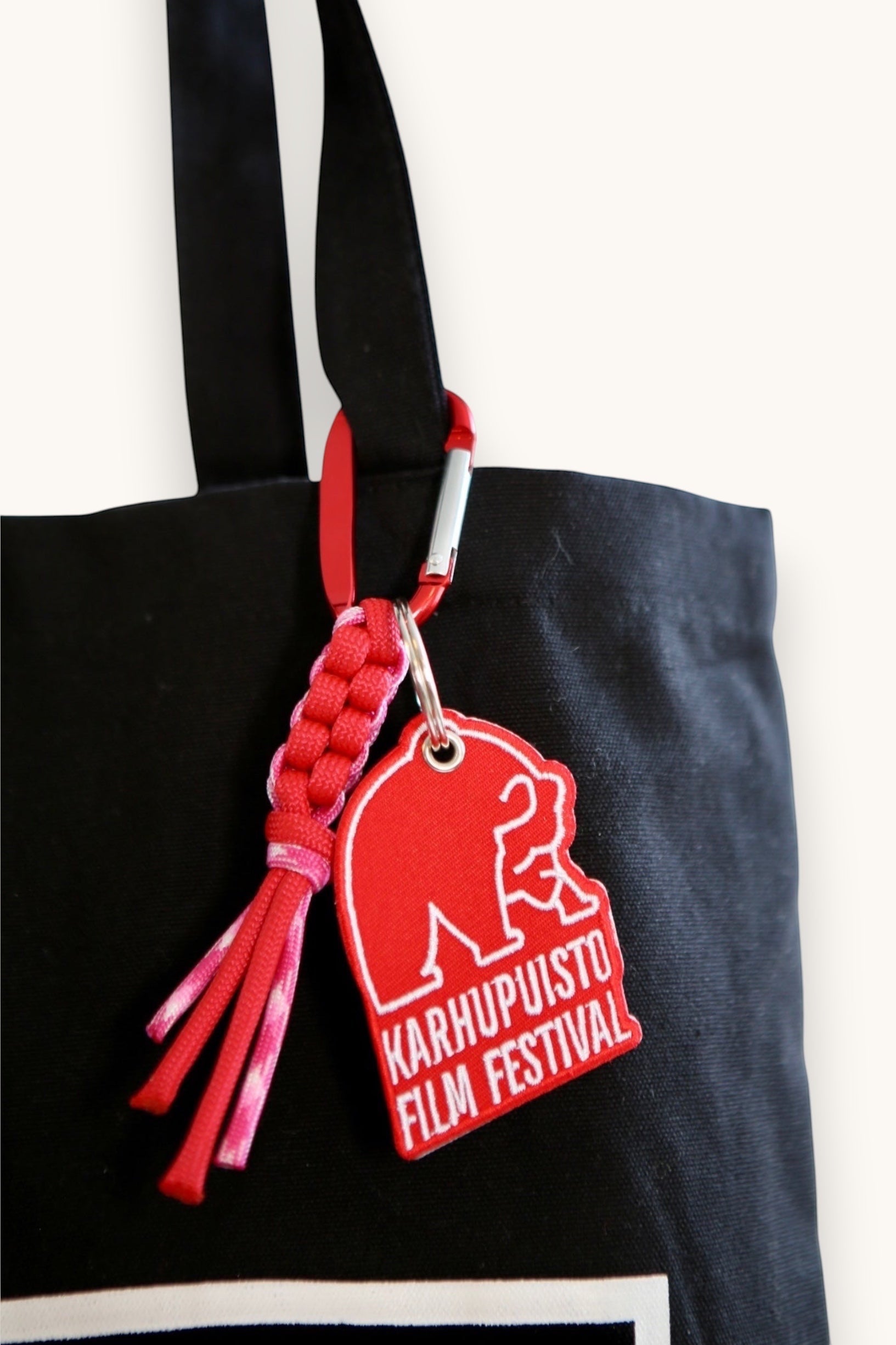 Karhupuisto Film Festival red bear keychain with paracord and carabiner clipped to a black tote bag.