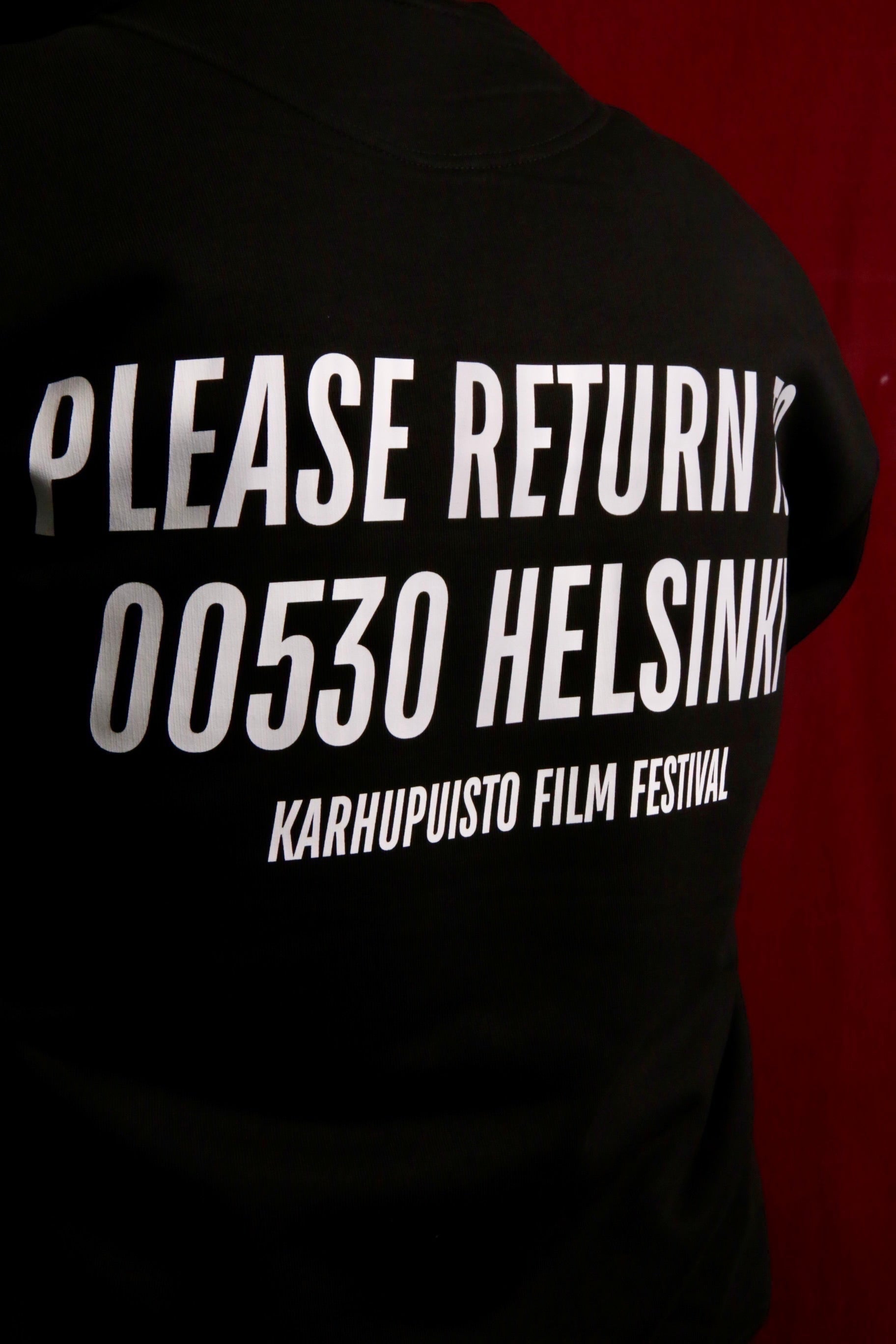 Karhupuisto Film Festival black unisex hoodie with white back print featuring Helsinki 00530 text