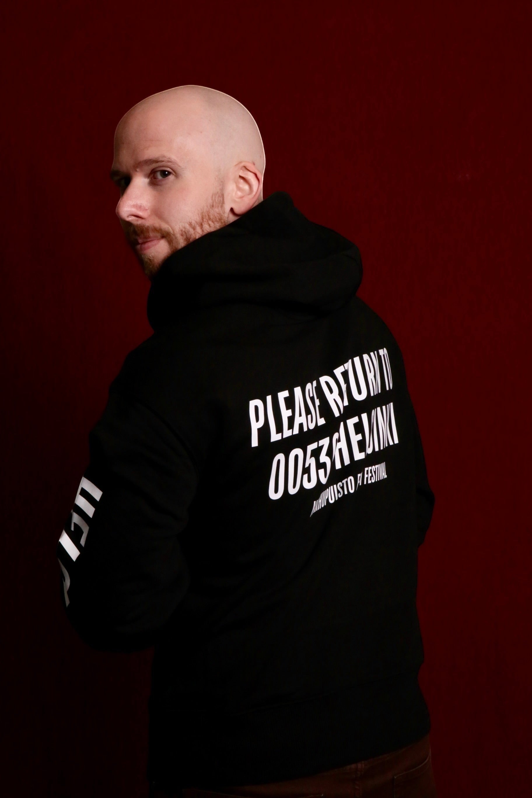 Karhupuisto Film Festival black unisex hoodie with white back print worn by a man against a dark red background