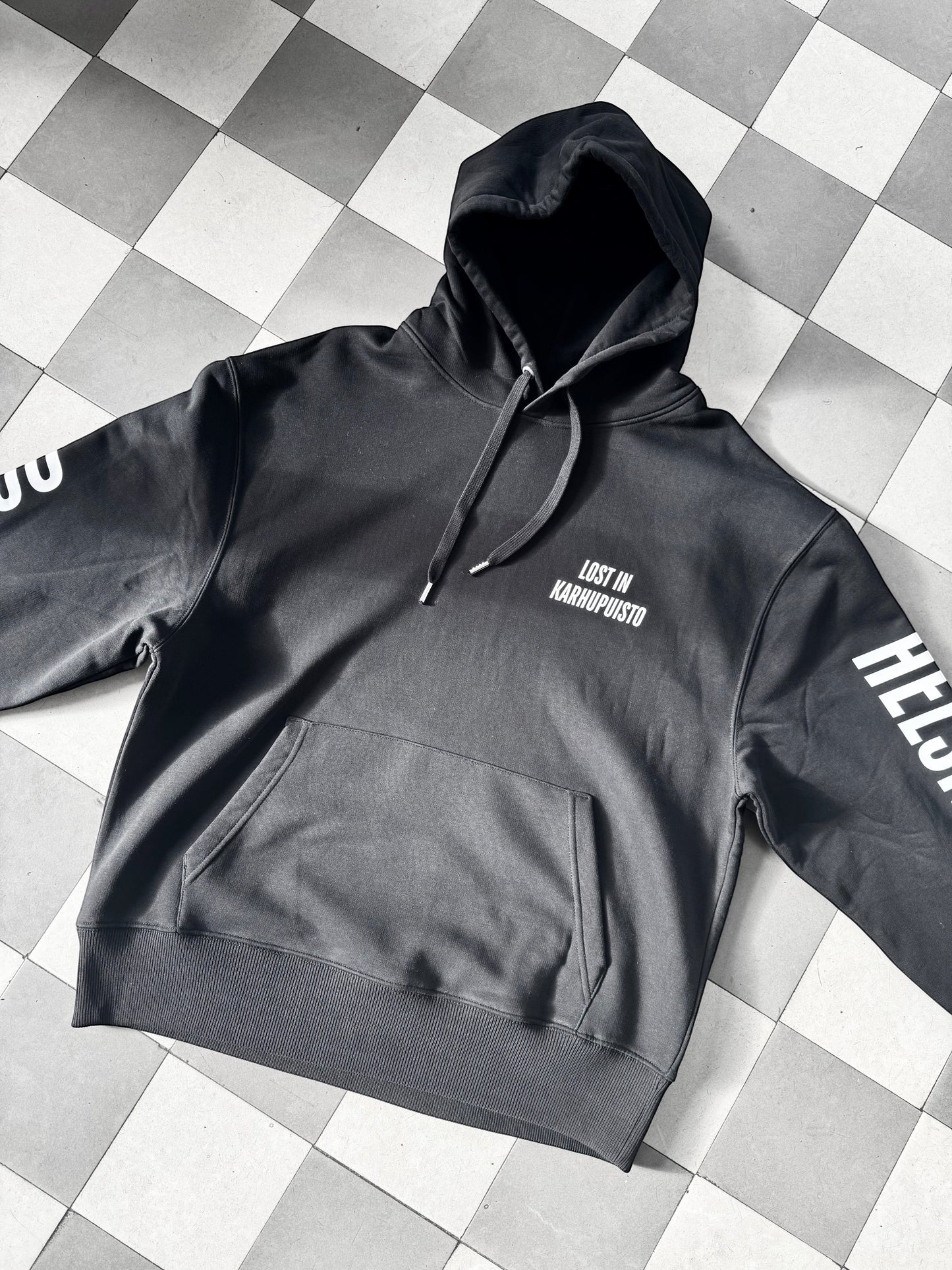 Karhupuisto Film Festival black unisex hoodie with white Lost in Karhupuisto print and Helsinki sleeve details.