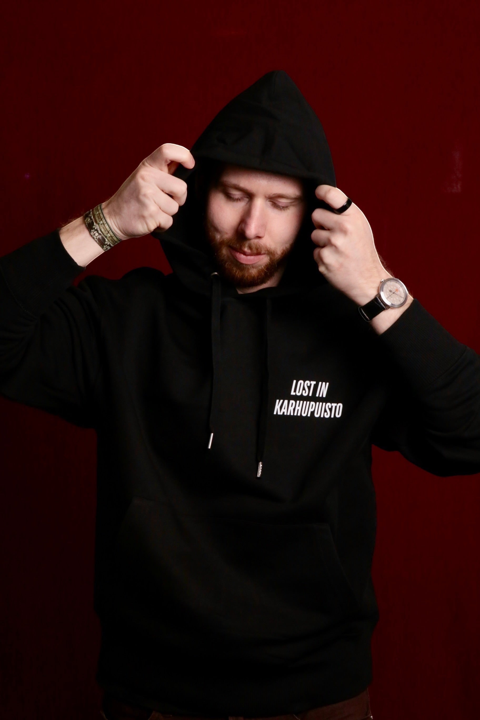 Karhupuisto Film Festival black unisex hoodie with Lost in Karhupuisto print worn by a man against a dark red background
