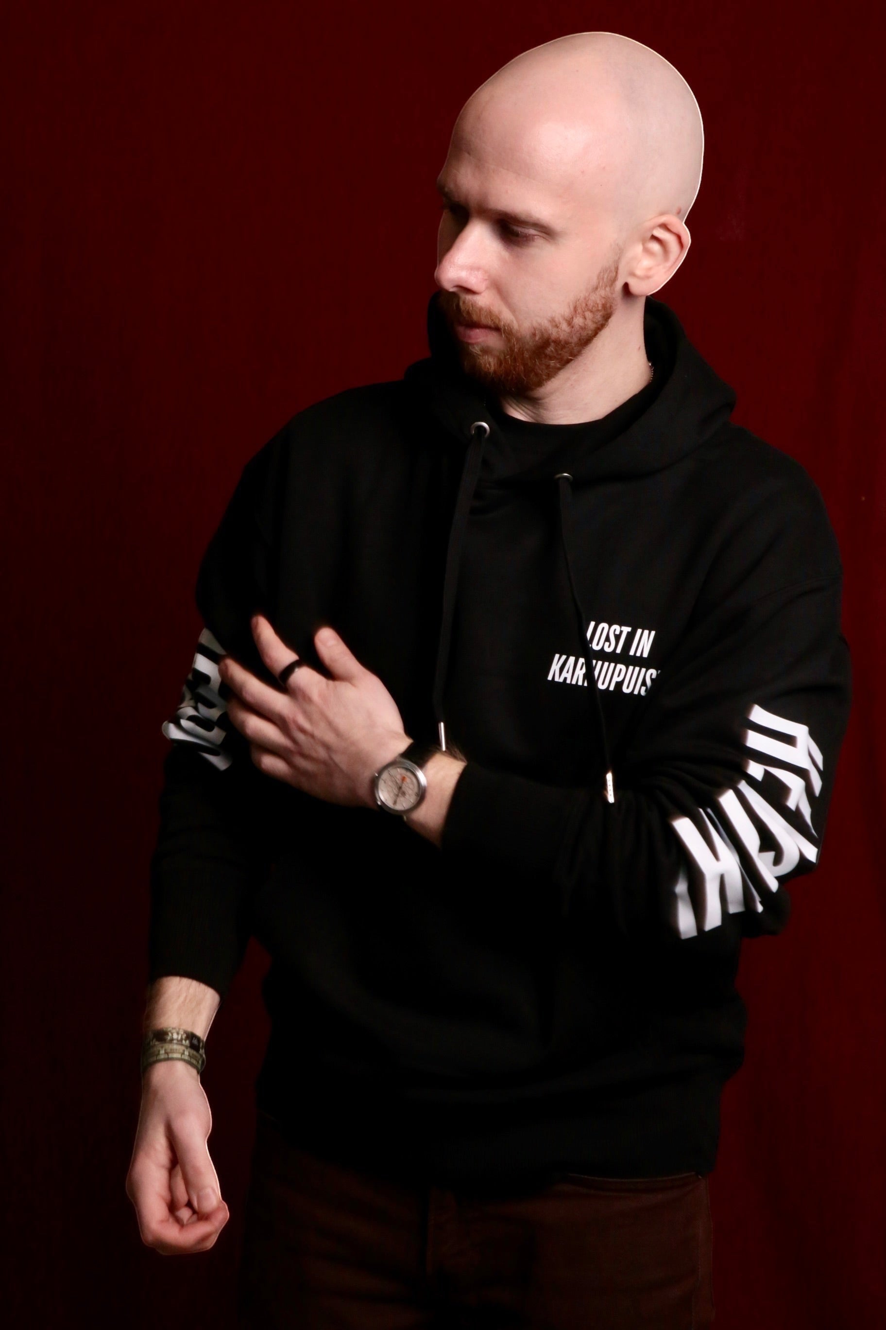 Karhupuisto Film Festival black unisex hoodie with white sleeve and chest text worn by a model against red background