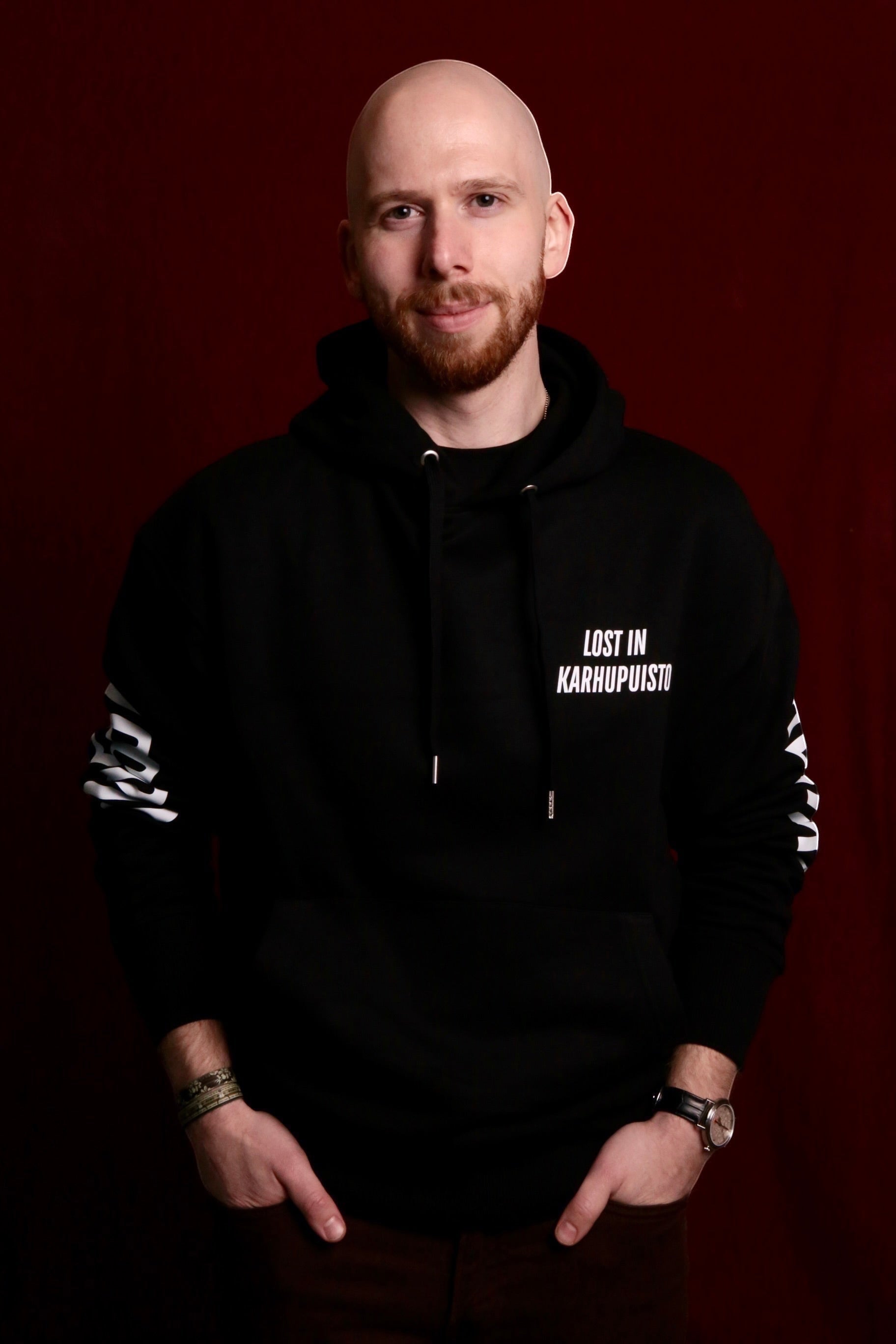 Karhupuisto Film Festival unisex black hoodie with Lost in Karhupuisto print worn by a man against a red background.