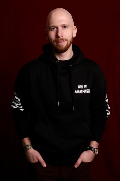 Karhupuisto Film Festival unisex black hoodie with Lost in Karhupuisto print worn by a man against a red background.