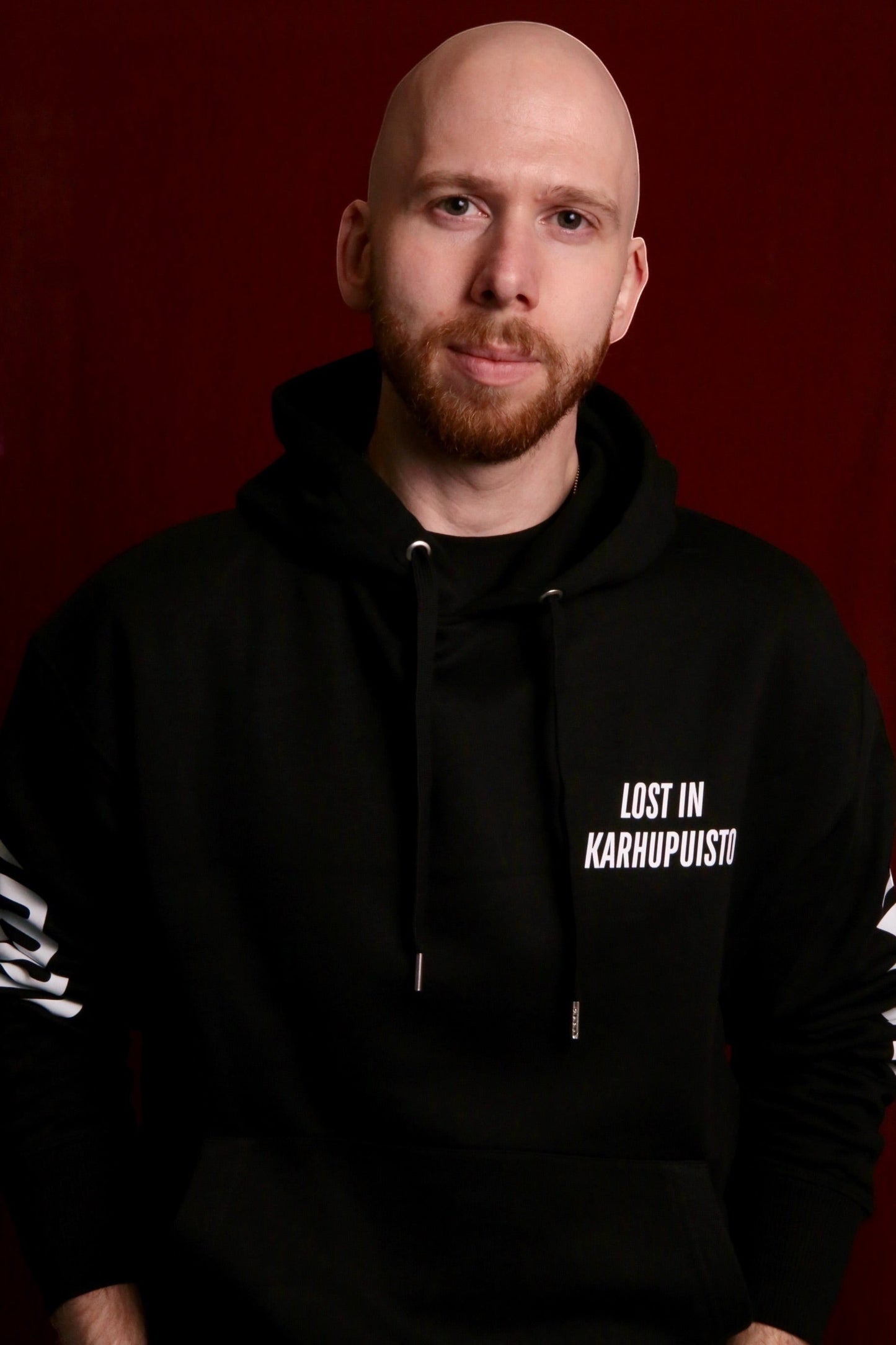 Karhupuisto Film Festival black unisex hoodie with white Lost in Karhupuisto chest print worn by a bearded man.