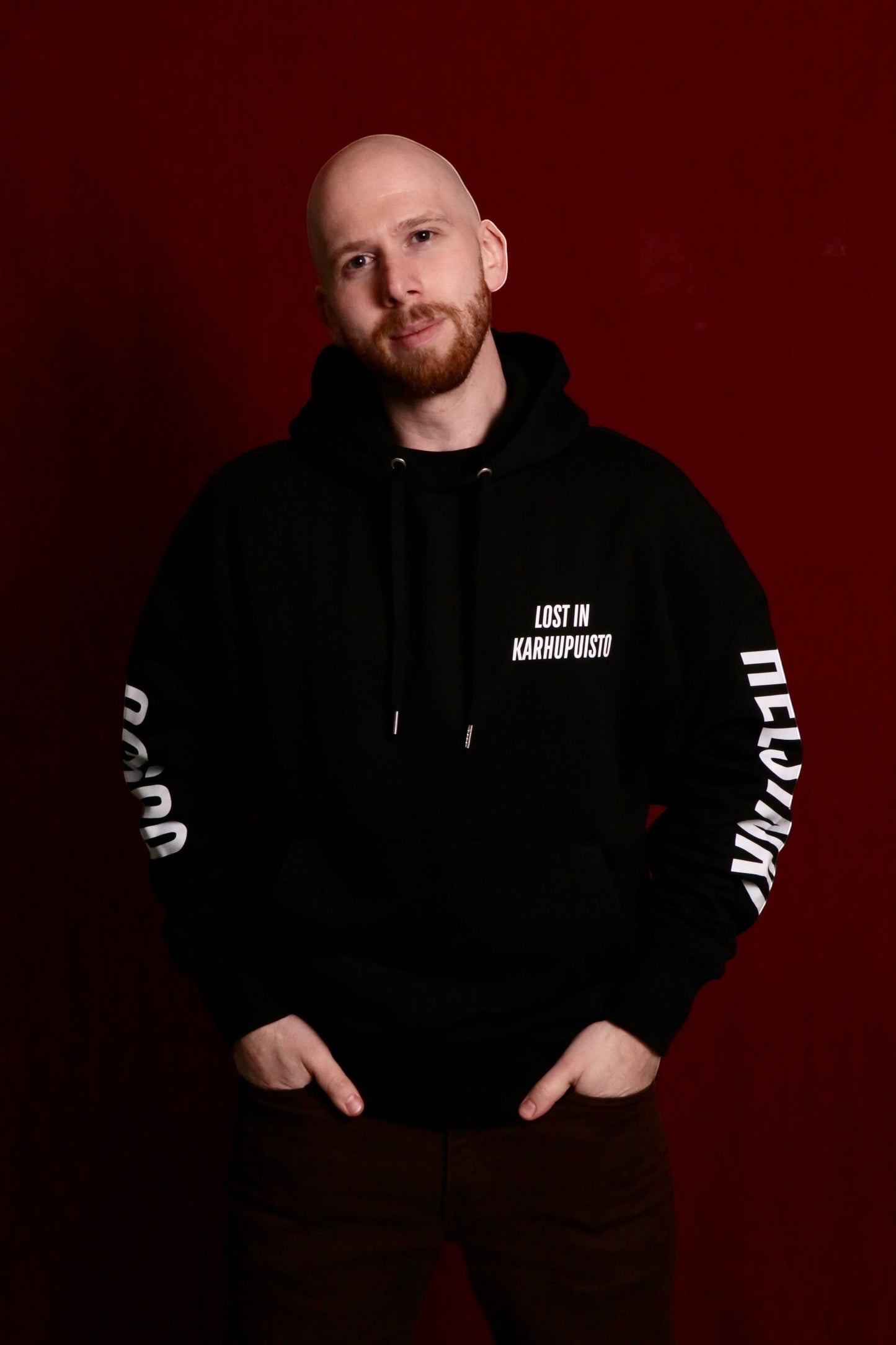 Karhupuisto Film Festival unisex black hoodie with white Lost in Karhupuisto print worn by a man against red background