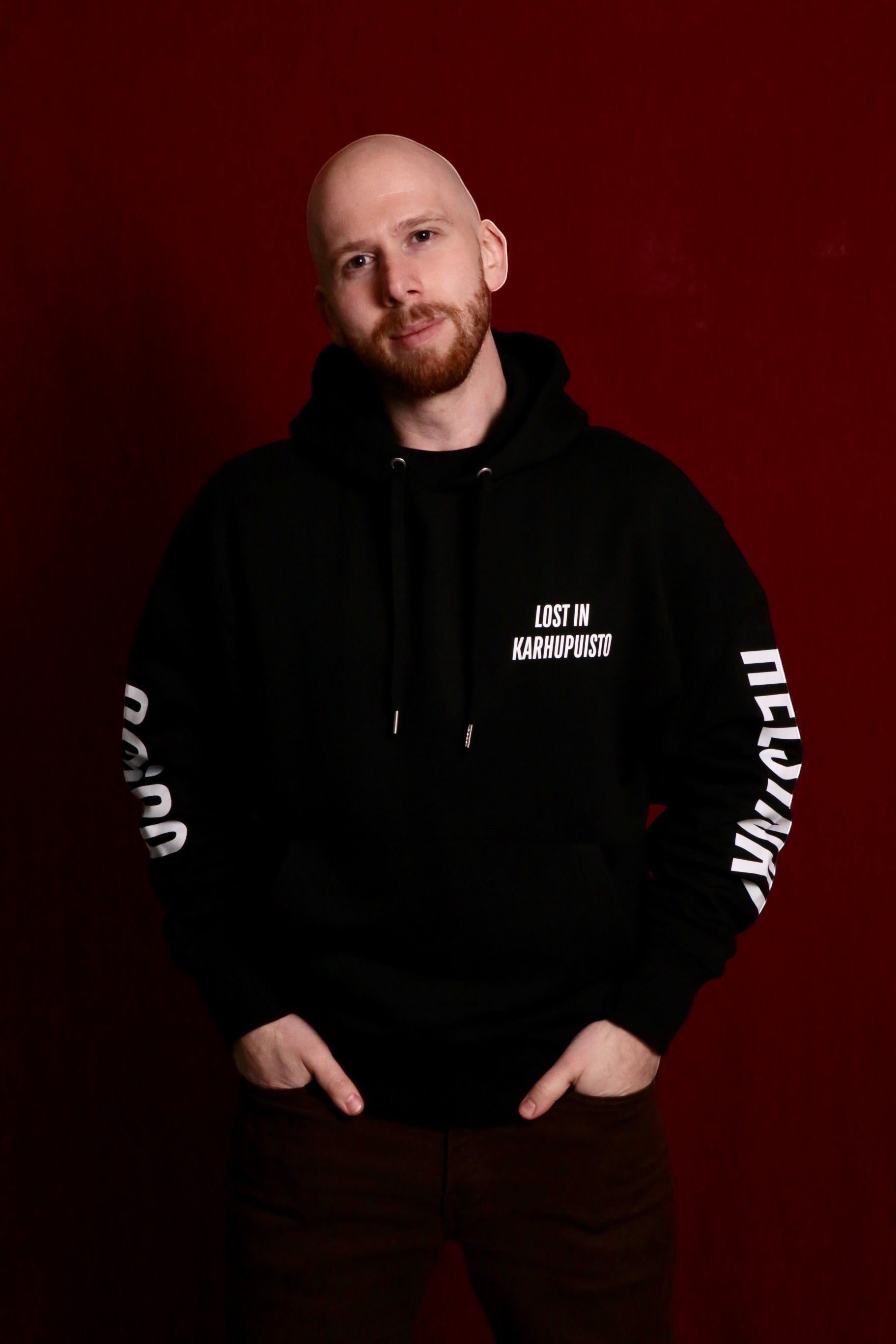 Karhupuisto Film Festival unisex black hoodie with white Lost in Karhupuisto print worn by a man against red background