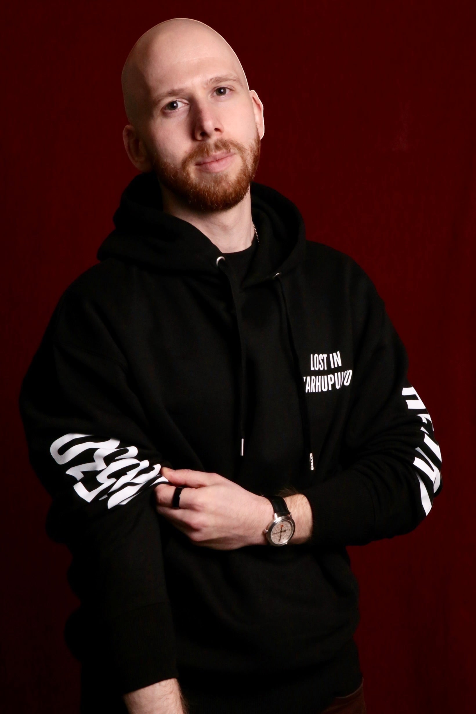 Karhupuisto Film Festival black unisex hoodie with white Lost in Karhupuisto print worn by a man against red background