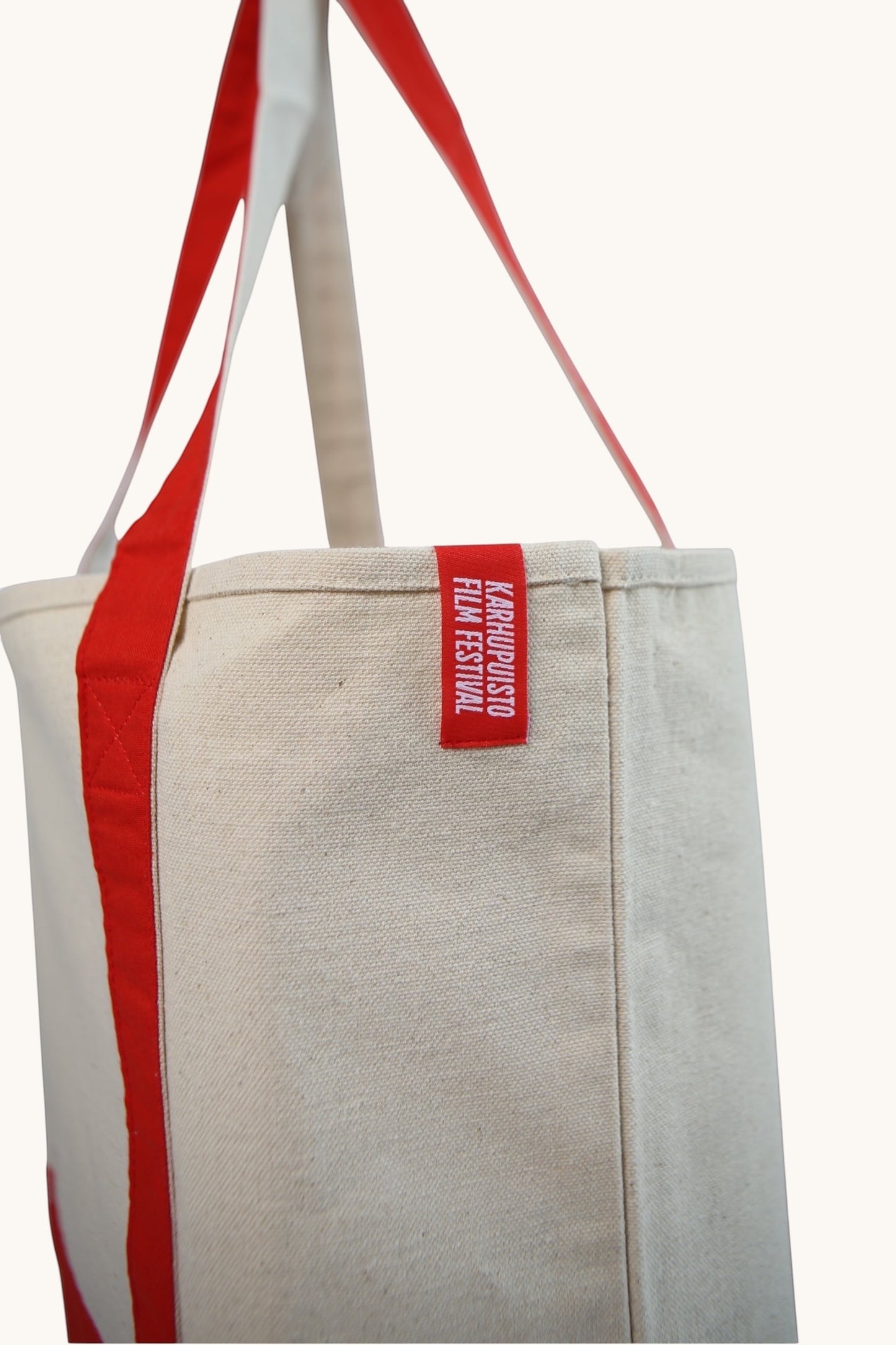 Karhupuisto Film Festival recycled cream cotton canvas tote bag with vibrant red shoulder straps and logo tag.