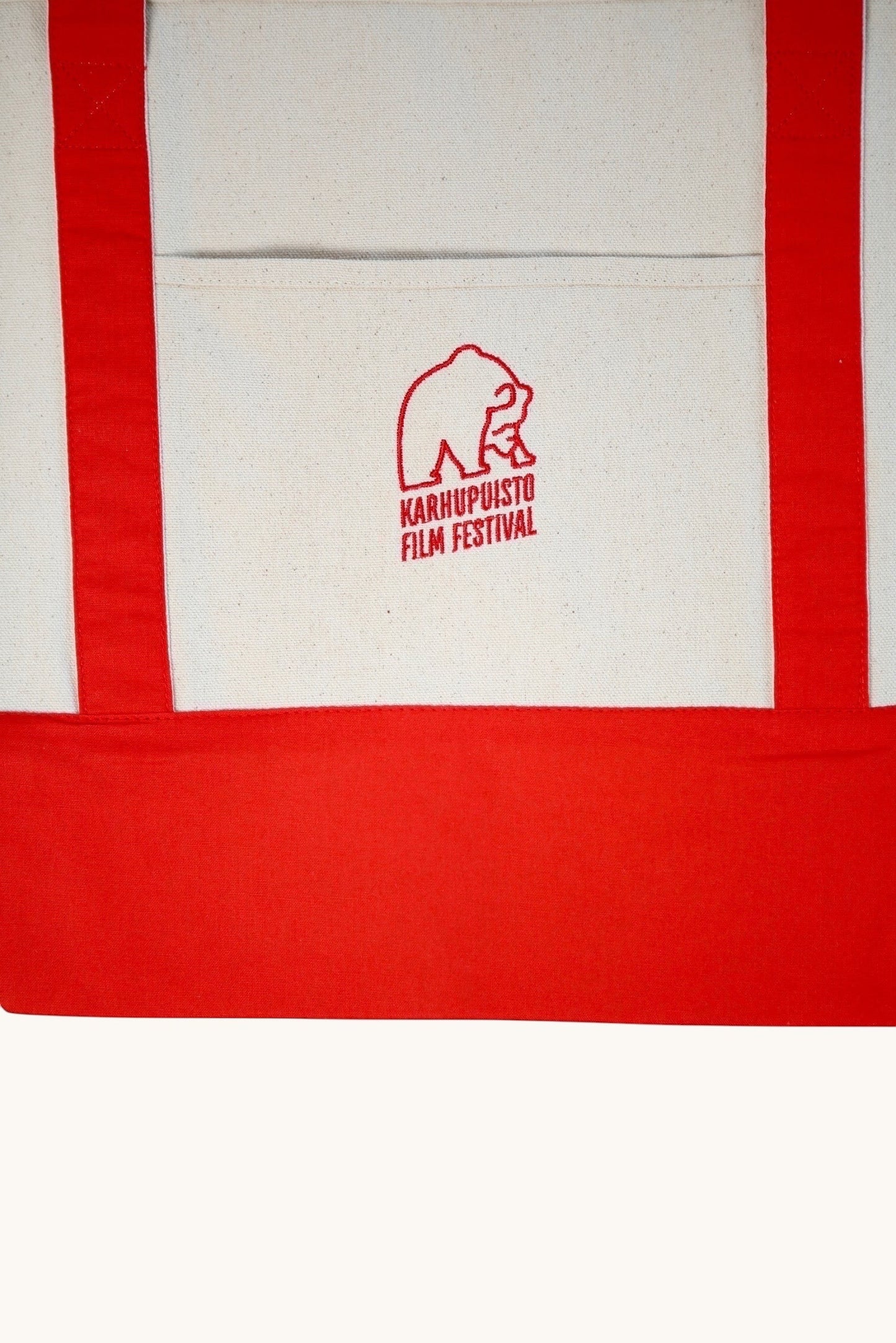 Karhupuisto Film Festival recycled cotton canvas tote bag in cream with red handles, base, and bear logo pocket.