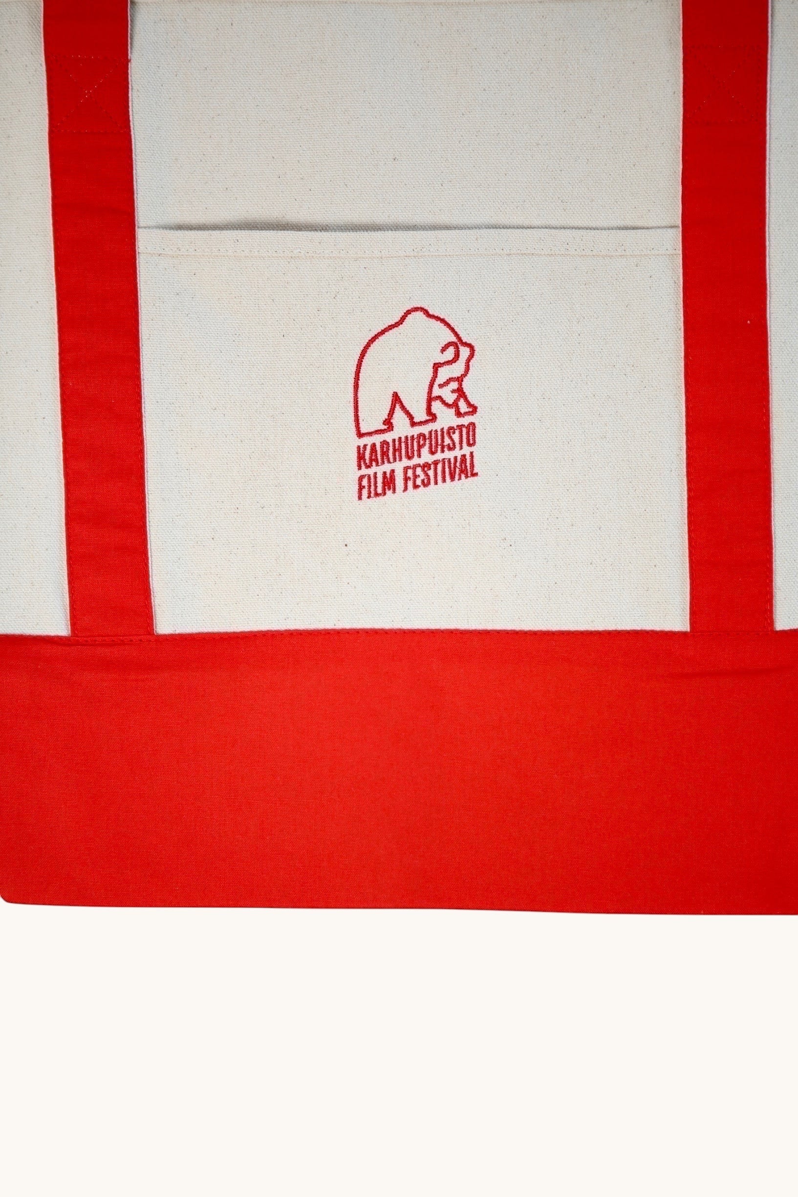 Karhupuisto Film Festival recycled cotton canvas tote bag in cream with red handles, base, and bear logo pocket.