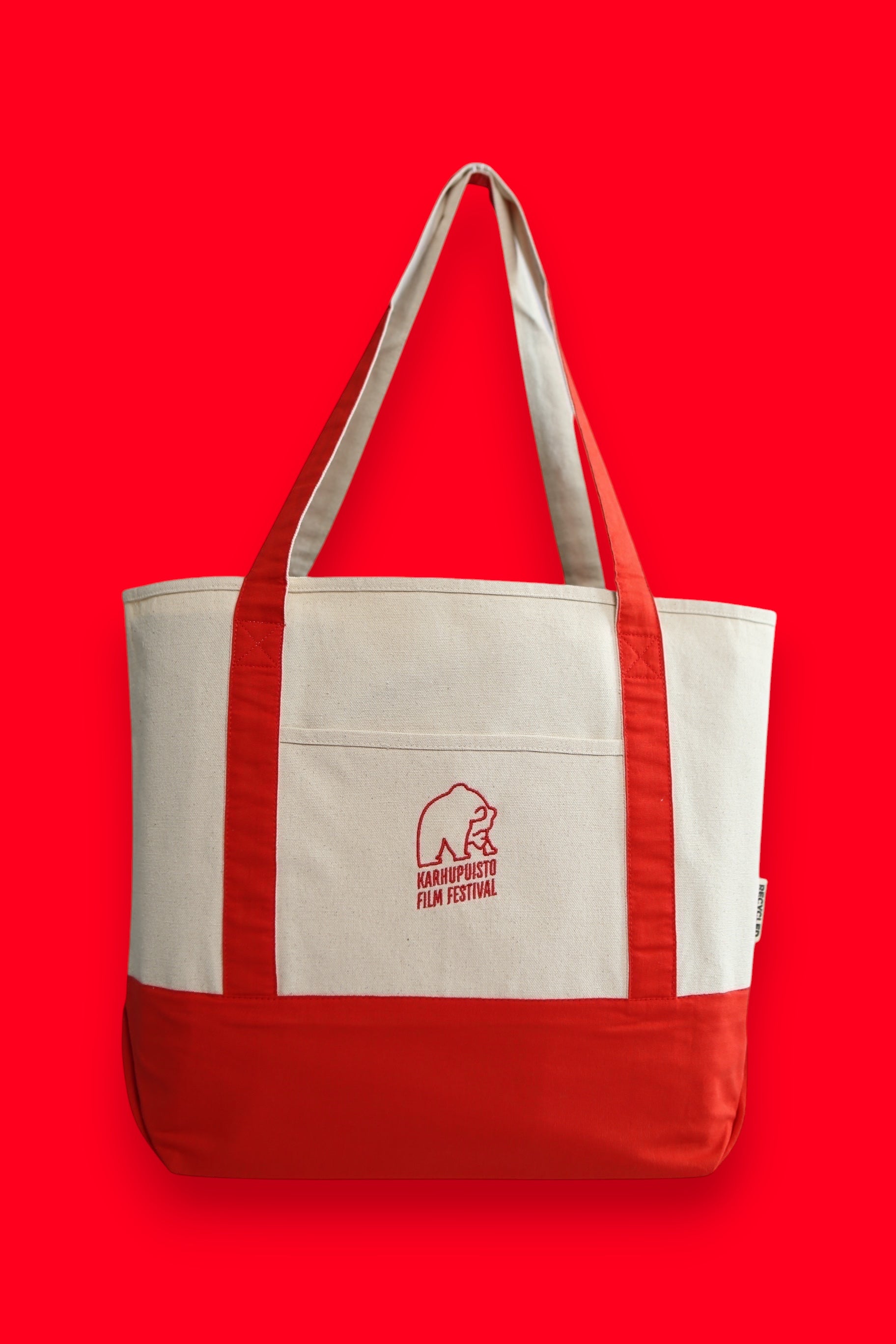 Karhupuisto Film Festival recycled cotton canvas tote bag in cream with red handles, base, and bear logo pocket.