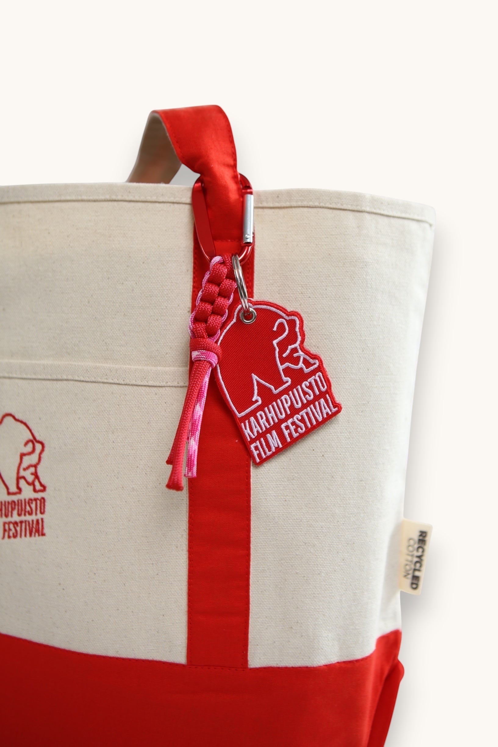 Karhupuisto Film Festival red bear keychain with paracord accent and carabiner clipped to a canvas tote bag