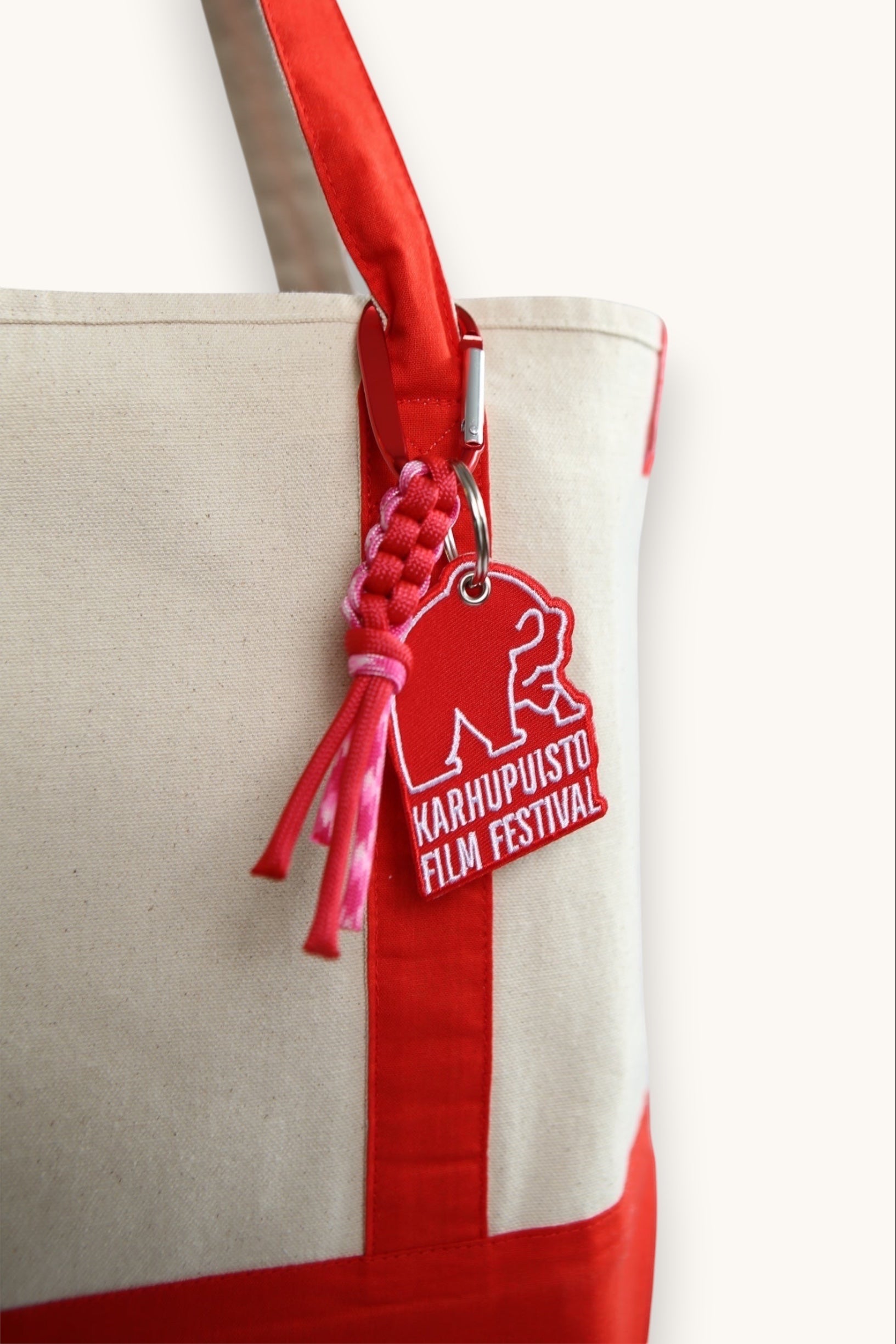 Karhupuisto Film Festival red bear keychain with pink paracord and carabiner attached to a canvas tote bag