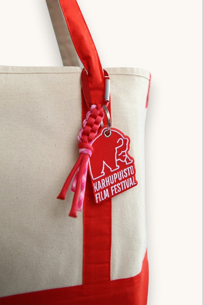 Karhupuisto Film Festival red bear keychain with pink paracord and carabiner attached to a canvas tote bag