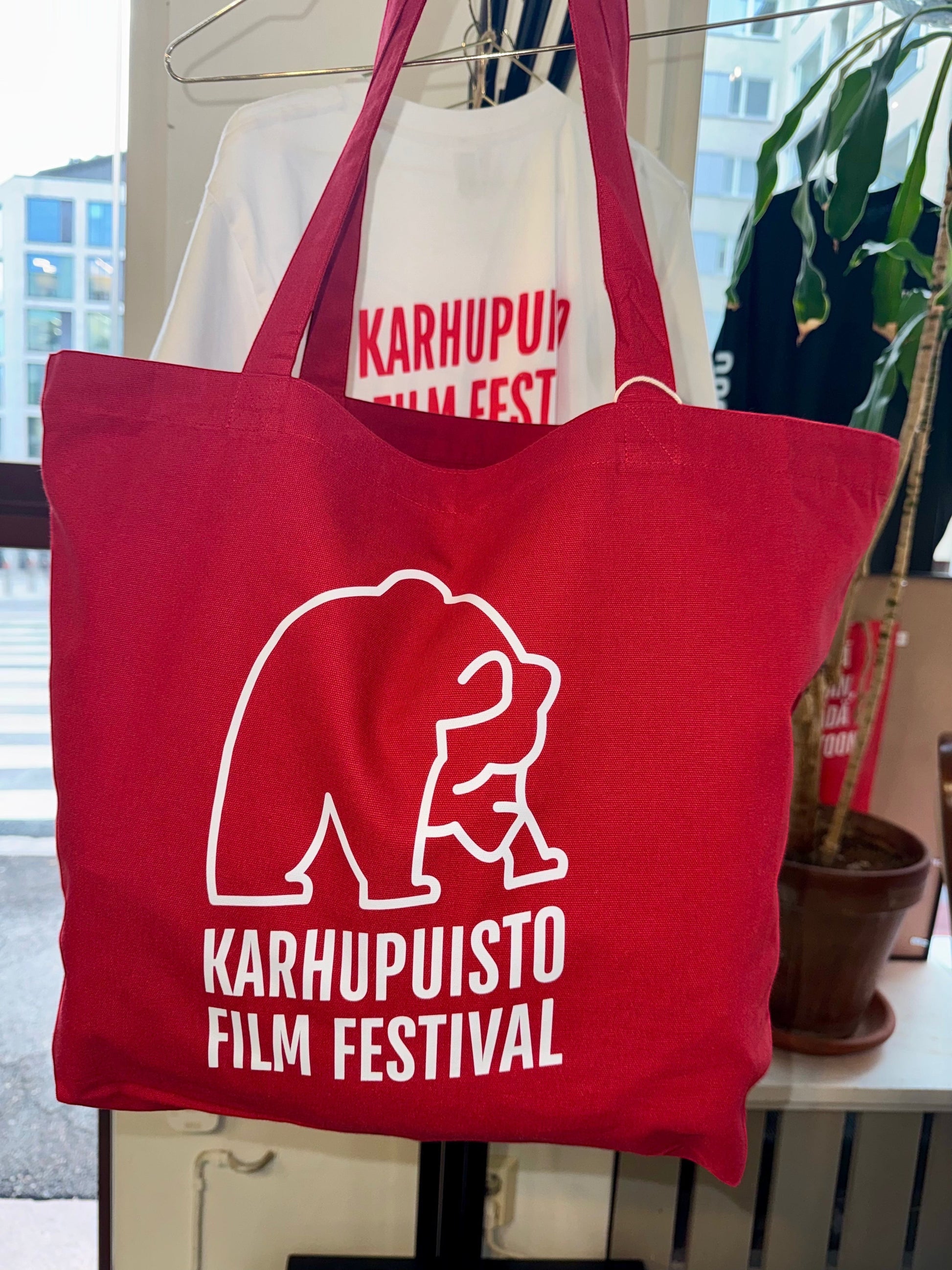 Karhupuisto Film Festival red cotton tote bag with white bear logo print hanging on a display rack