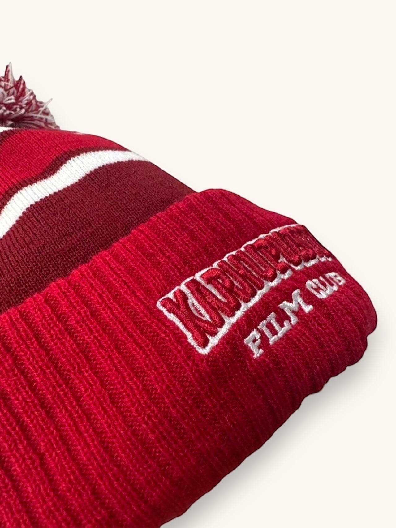 Karhupuisto Film Festival red and burgundy knit pom-pom beanie with white stripes and embroidered club logo