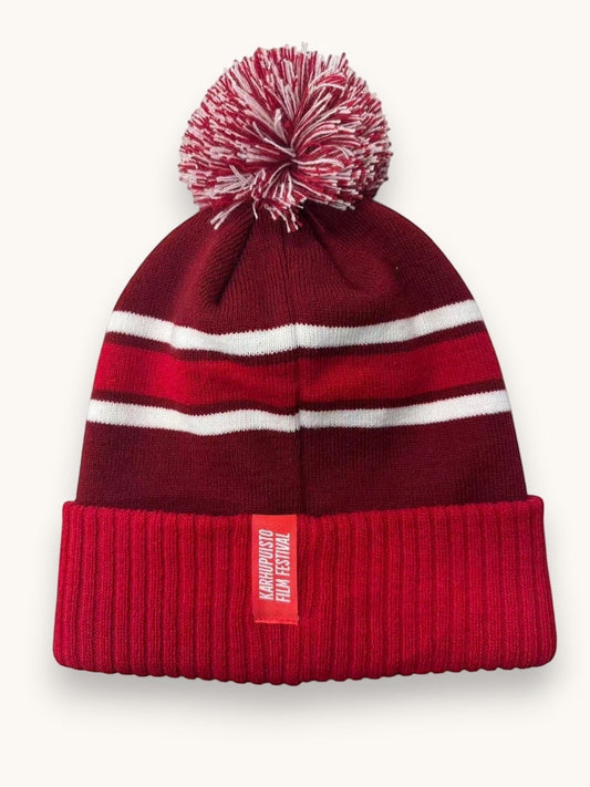 Karhupuisto Film Festival red and burgundy knit pom-pom beanie with white stripes and a ribbed cuff label.