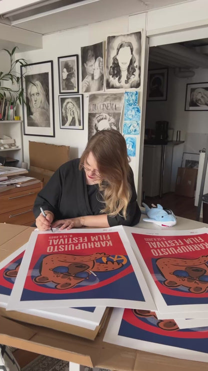 Taiteilija Taru Liikanen signeeraamassa Karhupuisto Film Festival taidejulisteita